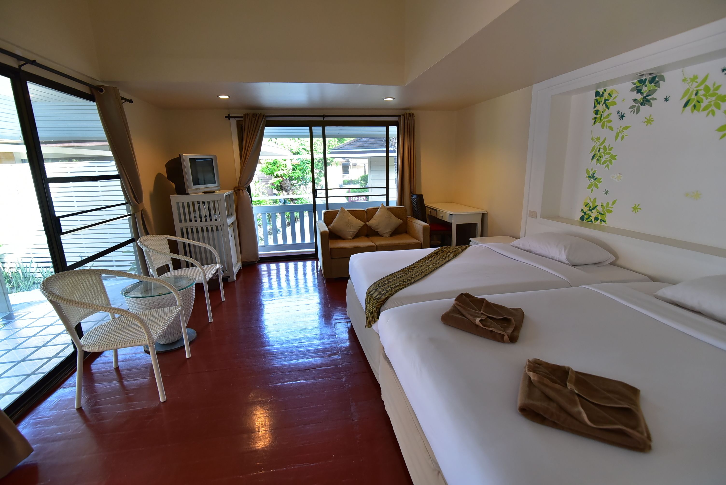 A hotel room with a large bed, a sofa, a TV, and a balcony with a view of the outside.
