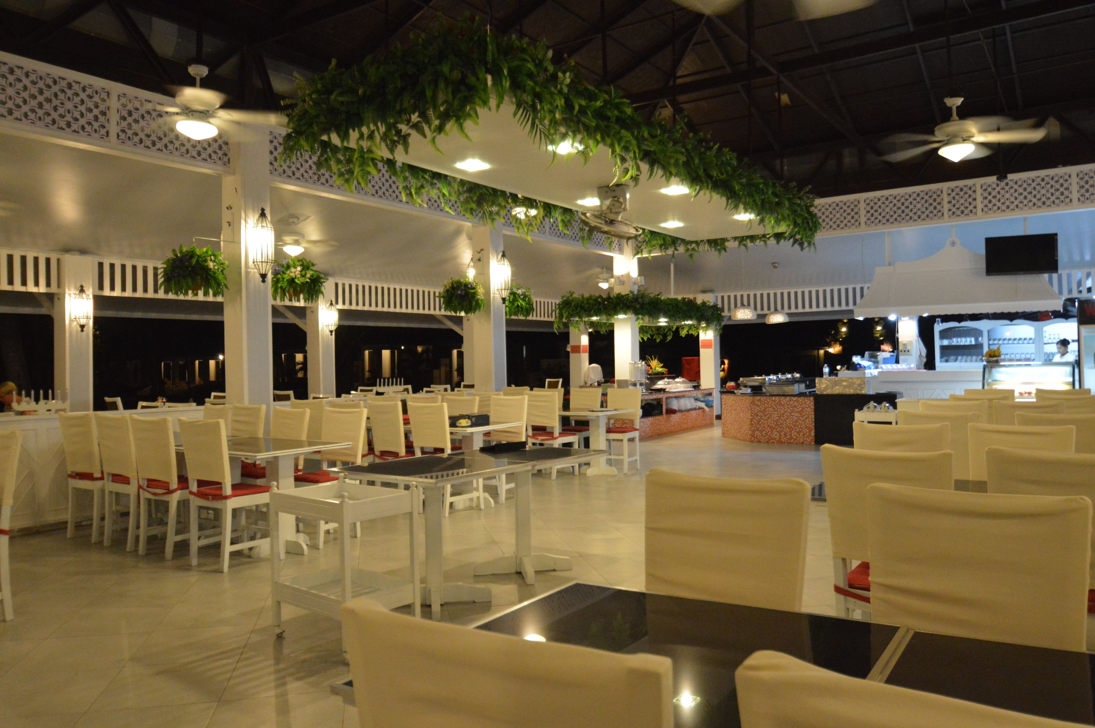 A spacious indoor area with multiple tables and chairs, ceiling fans, and hanging plants.