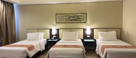 Habitación de hotel con tres camas, cada una con ropa blanca y una manta marrón. Hay mesitas de noche con lámparas y un teléfono en la pared. Encima de las camas, un cuadro enmarcado.