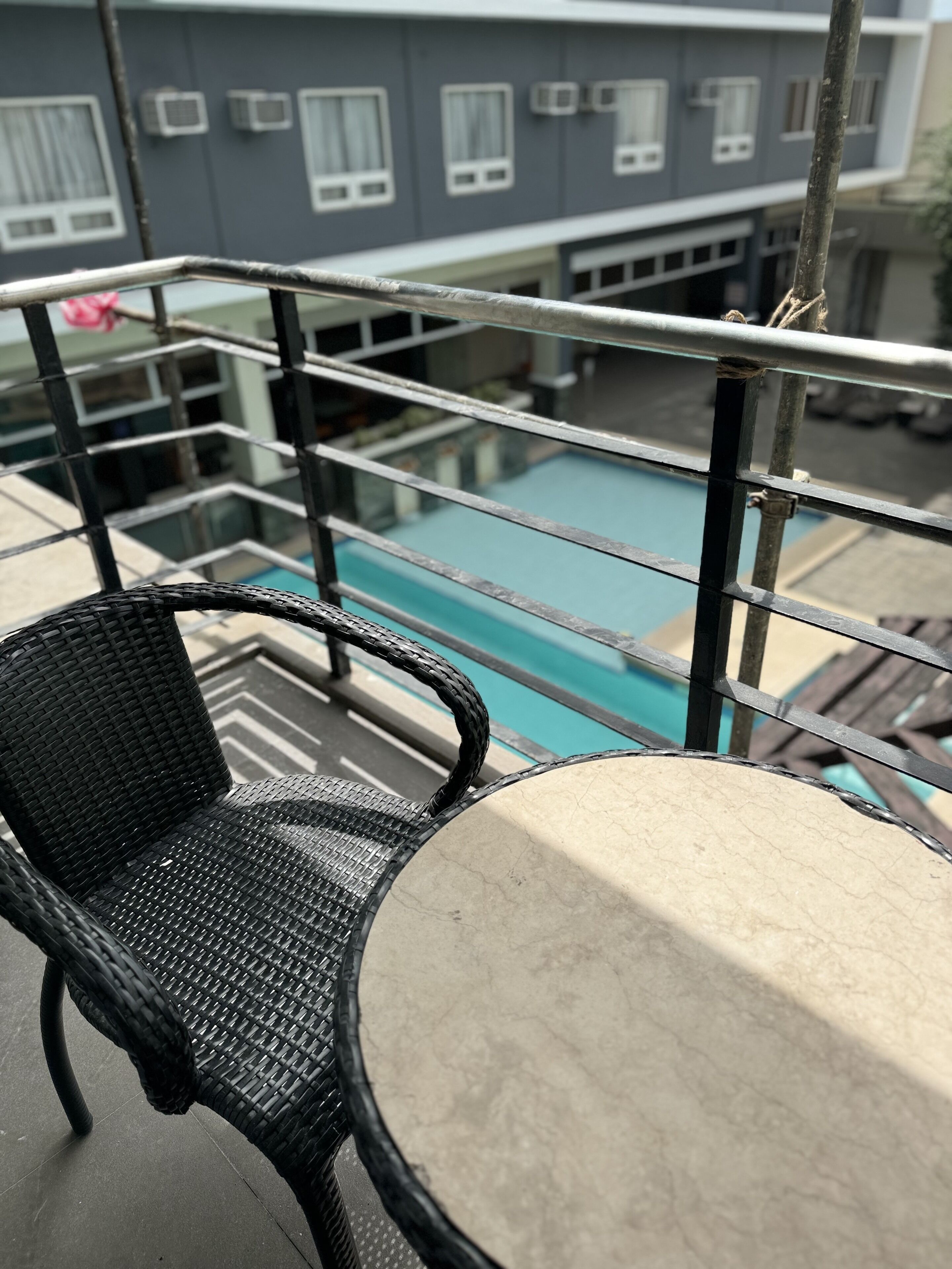 Un balcón con vista a una piscina, una silla de mimbre y una mesa.