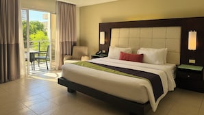A hotel room with a large bed, a nightstand, a chair, and a view of greenery through the window. - Circle Inn - Iloilo City Center (Iloilo)