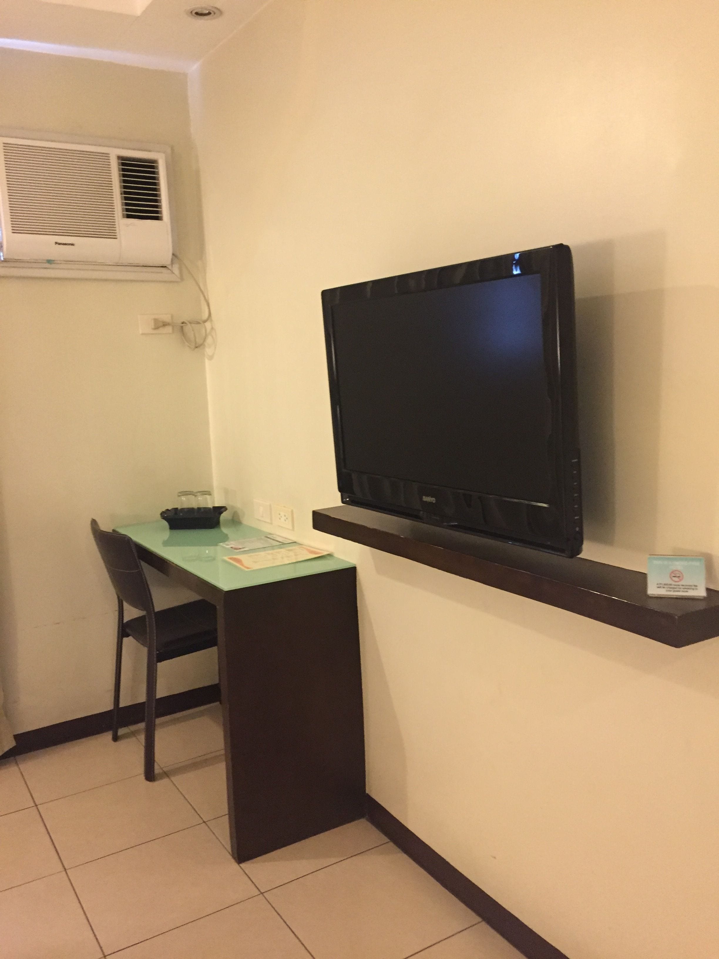 A small room with a desk, chair, and a mounted flat-screen TV.