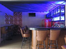 Zona de bar con mostrador, taburetes y una estantería con botellas.