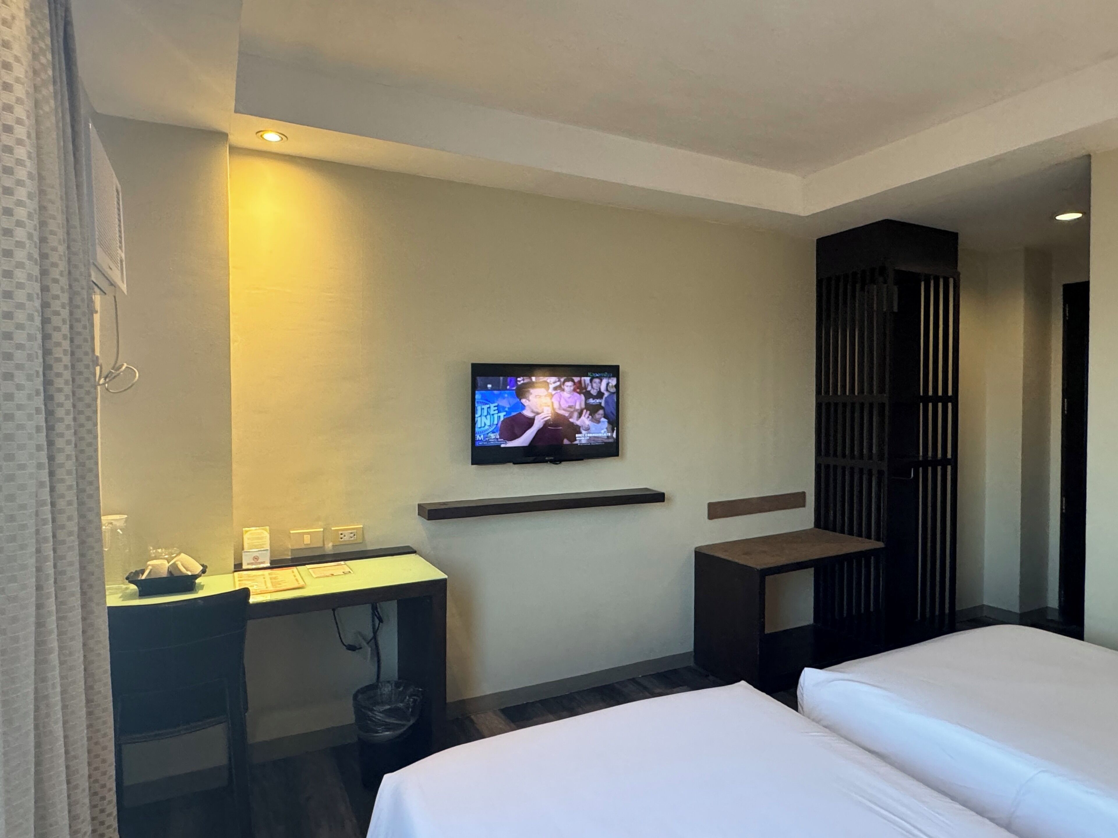 A hotel room with a bed, a desk, a TV mounted on the wall, and a small table.