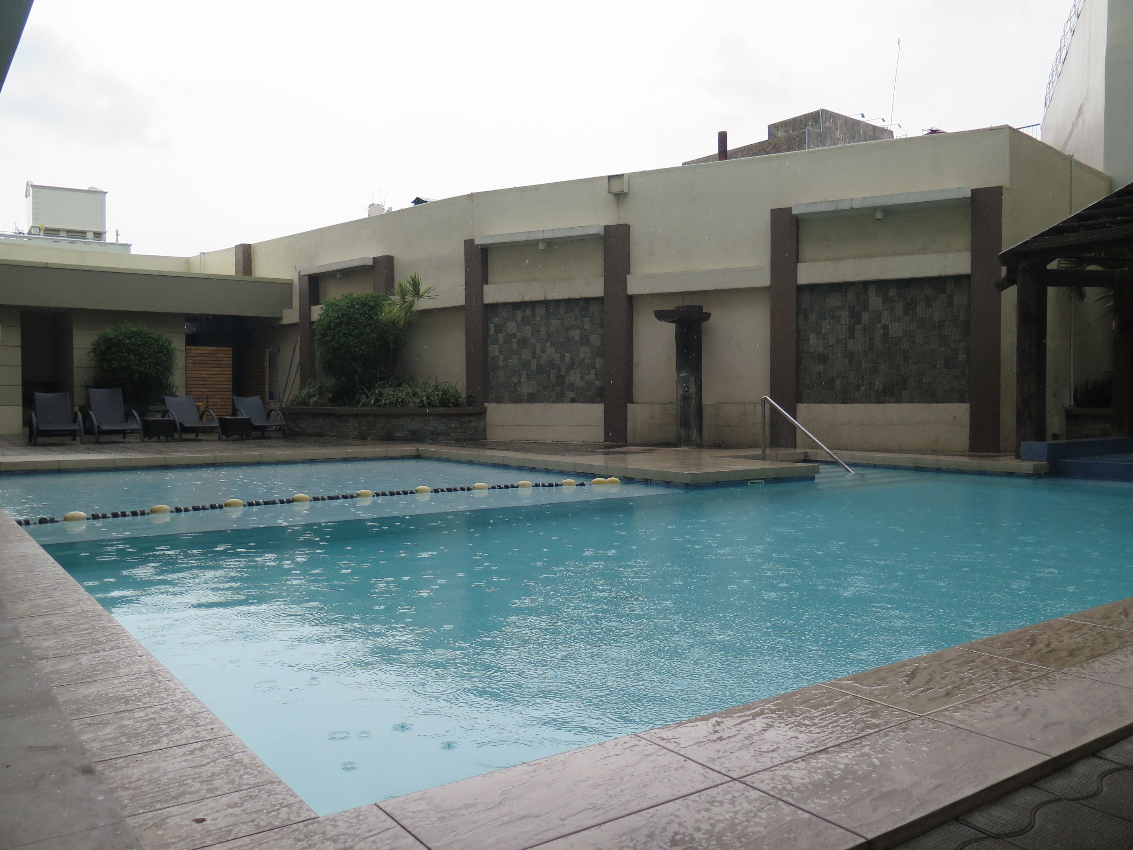 A swimming pool with a tiled deck, lounge chairs, and a building with a stone facade.