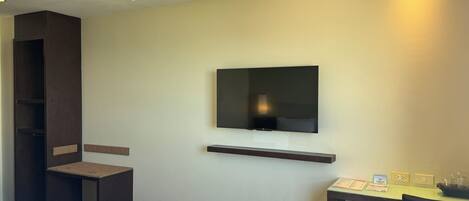 Egy szállodai szoba, amelyben található egy ágy, egy íróasztal széssel, egy falra szerelt televízió, és egy kis polc a televízió alatt.