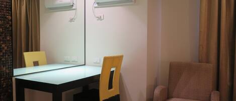 A hotel room with a dining table, two chairs, a sofa, and two wall-mounted air conditioning units.