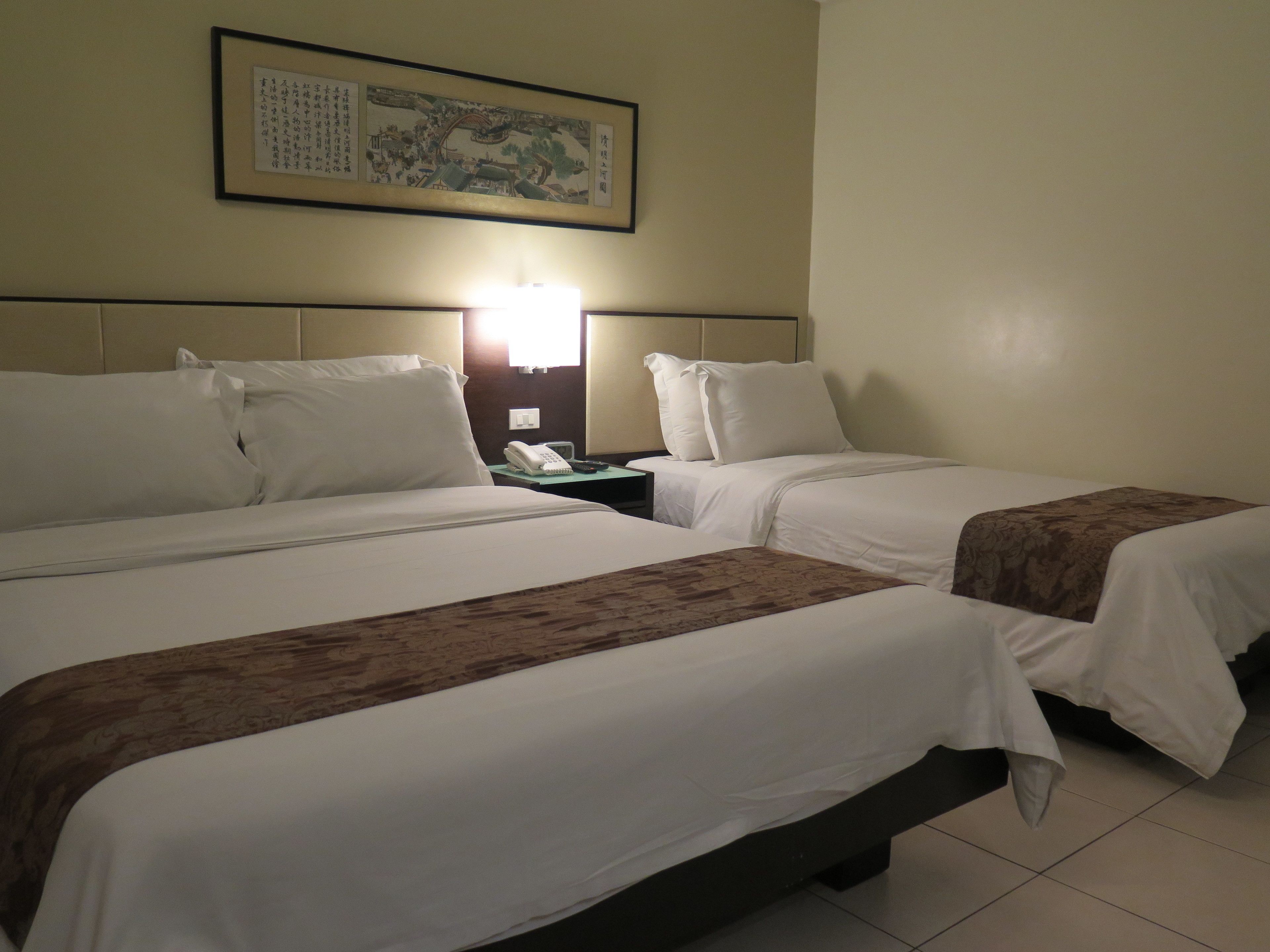 A hotel room with two beds, a nightstand with a phone, and a wall-mounted artwork.