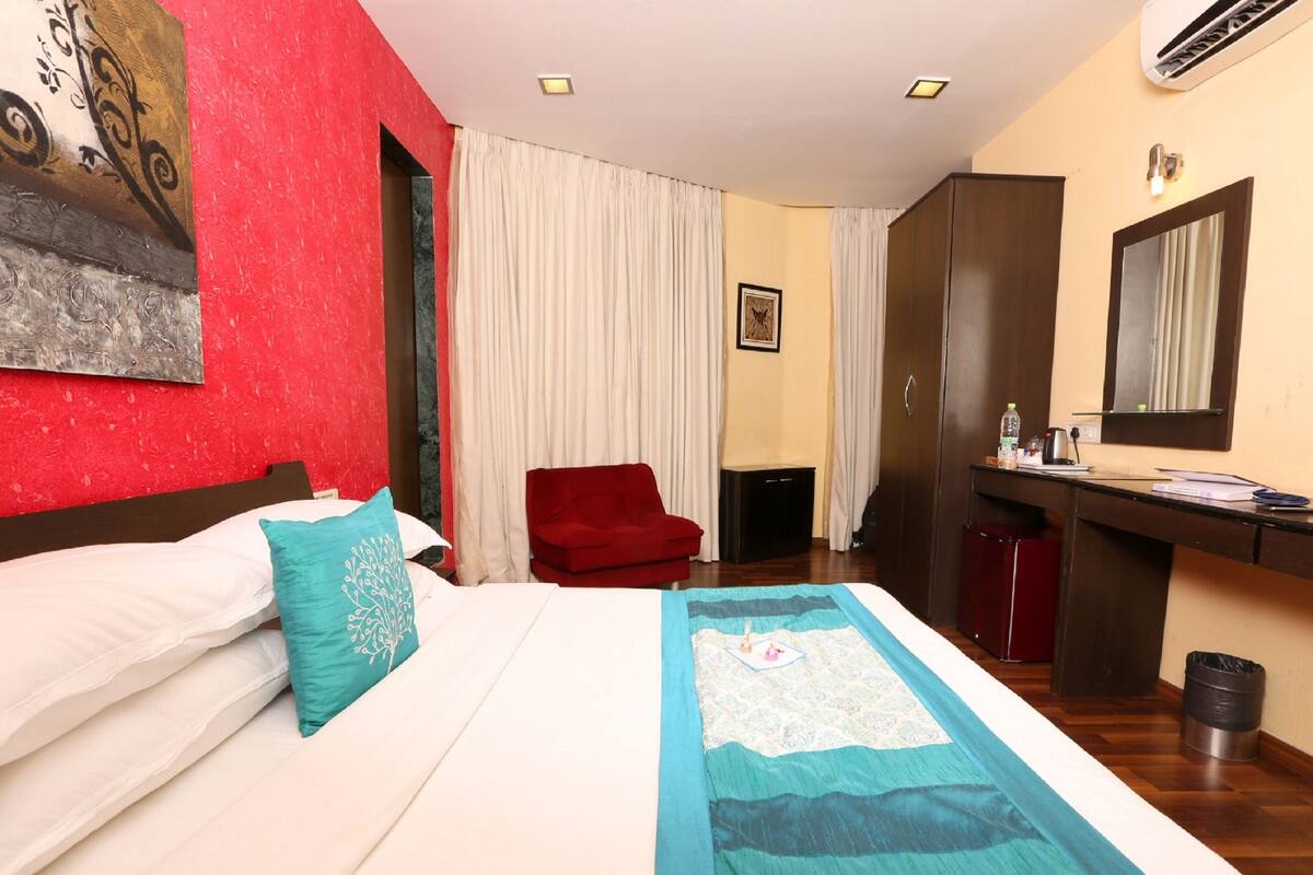 Habitación de hotel con cama, escritorio, silla, armario y espejo.