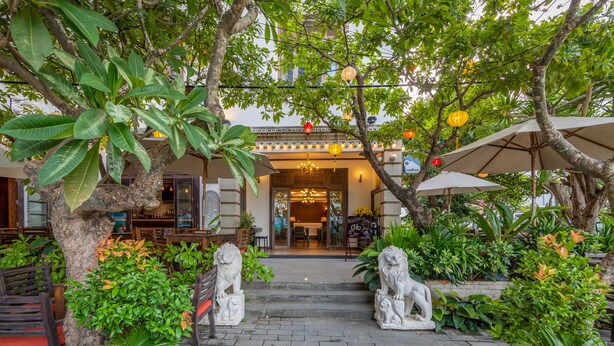 An outdoor entrance with stone lion statues, potted plants, and outdoor seating. - Chu Hotel (Da Nang)