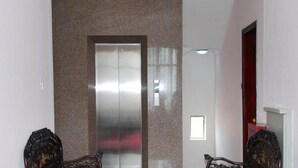 A hallway with a marble wall, a double elevator door, and a door with a red frame. - Areca Hotel (Hue)
