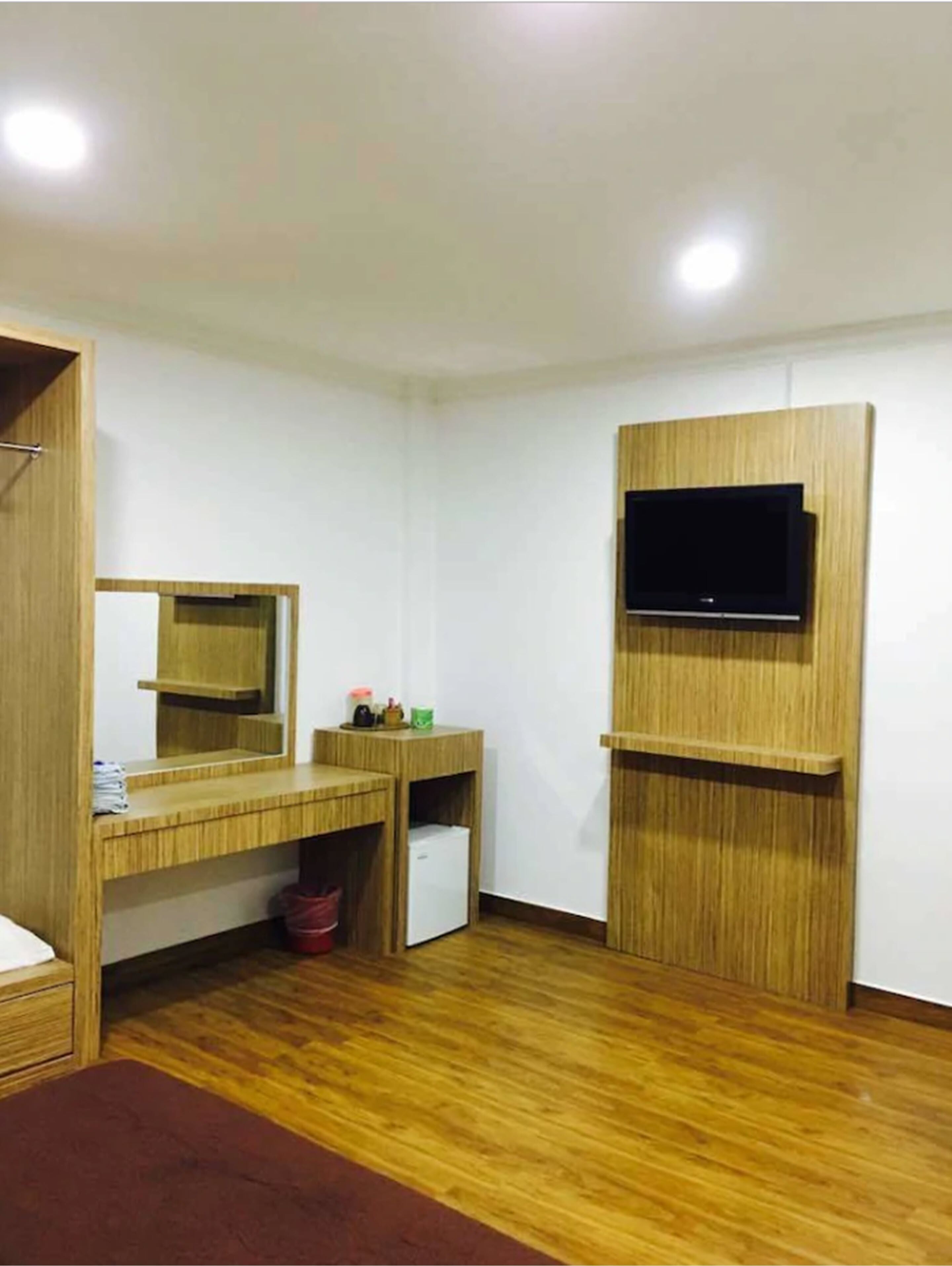 A room with a wooden vanity, a mirror, a small refrigerator, and a mounted TV.