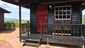 A wooden building with a red door, a window with white trim, and a porch with steps and railings. - Landcons Hotel (Langkawi)