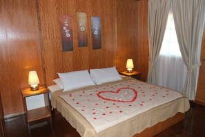 A neatly made bed with a heart-shaped decoration, two bedside lamps, and wooden paneling on the walls. - Landcons Hotel (Langkawi)