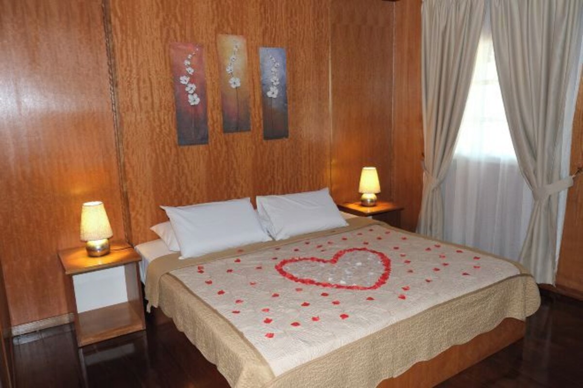 A neatly made bed with a heart-shaped decoration on the bedspread, two bedside lamps, and wooden paneling on the walls.
