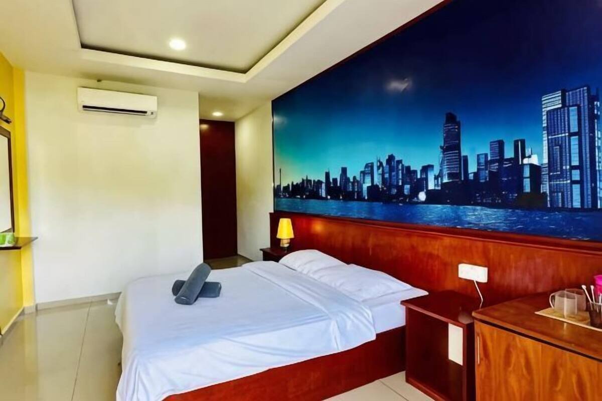A hotel room with a bed, a nightstand, a desk, a cityscape mural, and an air conditioning unit.