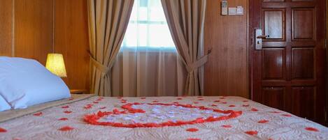A hotel room with a bed, curtains, a wooden door, and a window with curtains.