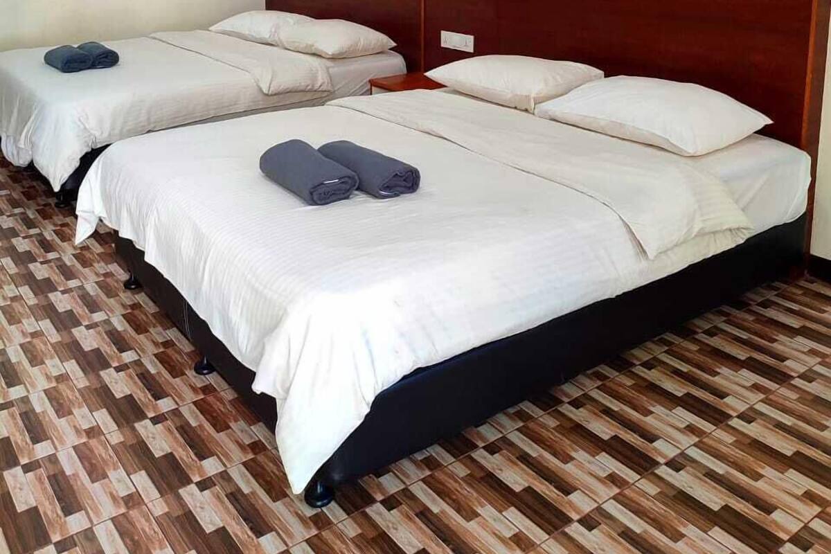 A hotel room with two beds, a wooden headboard, a patterned floor, and an air conditioning unit on the wall.