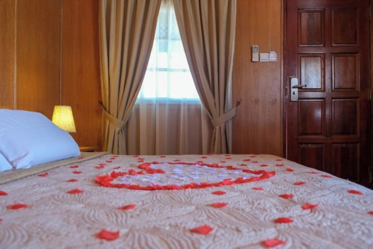 A hotel room with a bed covered in a patterned bedspread, a bedside lamp, and a wooden door.