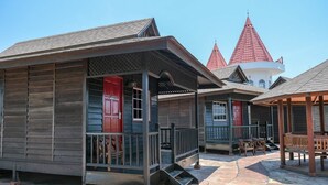 A row of wooden cabins with red doors, a covered porch, and a stone pathway. - Landcons Hotel (Langkawi)