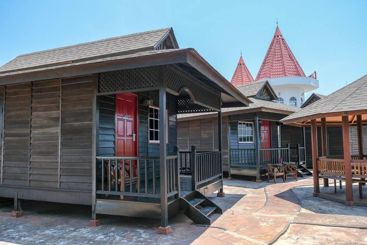 A row of wooden cabins with red doors, a covered porch, and a stone pathway.