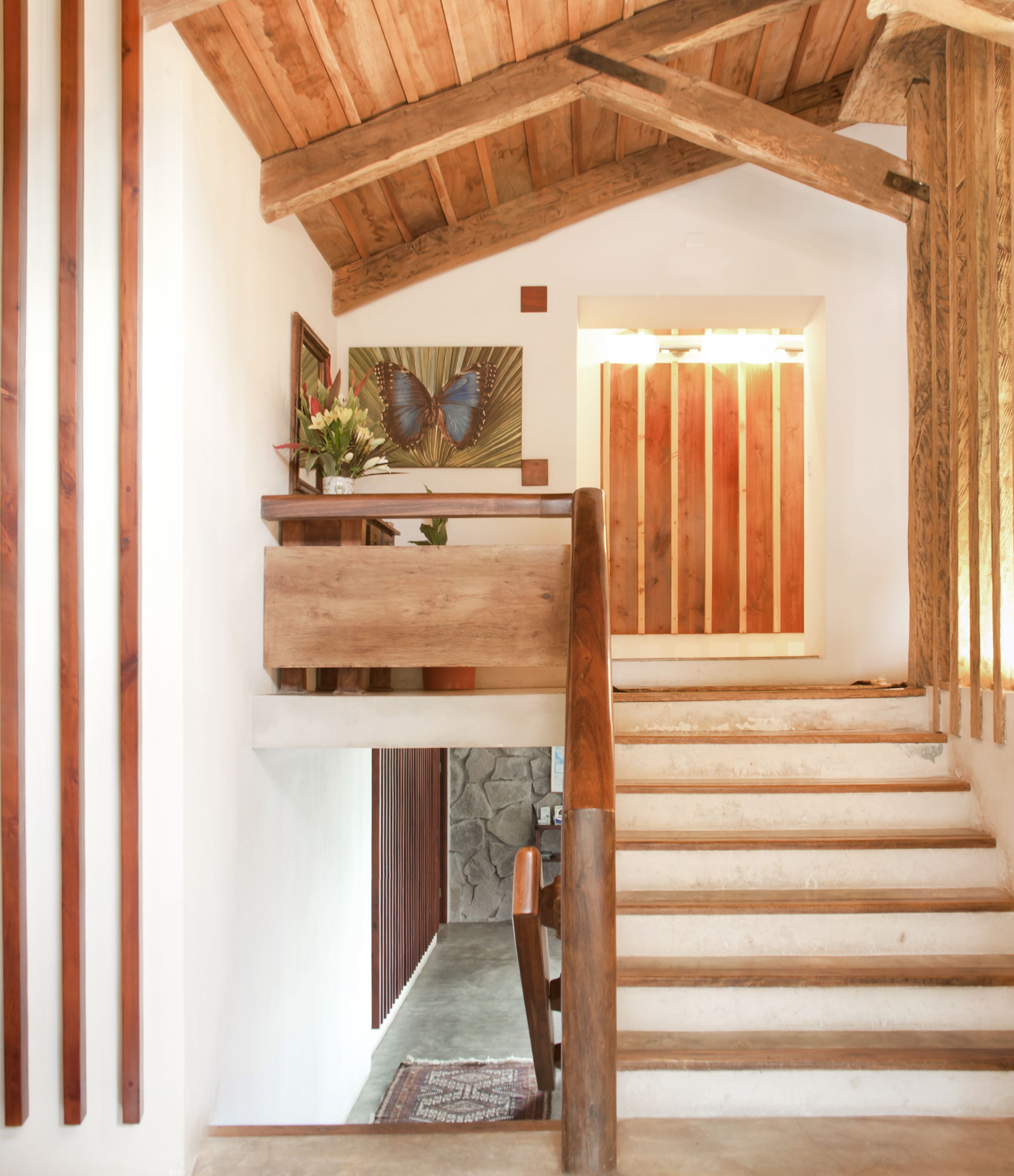A wooden staircase with a stone wall at the bottom, a wooden railing, and a butterfly painting on the wall.