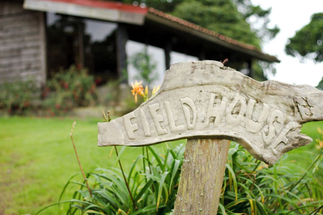 A wooden signpost with the inscription "FIELD HOUSE" in a garden setting.