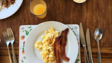 Un plato de desayuno con huevos revueltos y tocino, un vaso de jugo de naranja y un plato de cereal con leche.