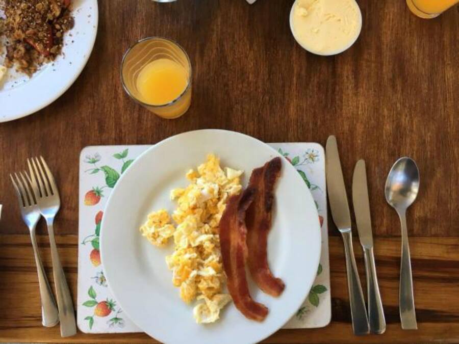 Un plato de desayuno con huevos revueltos y tocino, un vaso de jugo de naranja y un plato de cereal con leche.