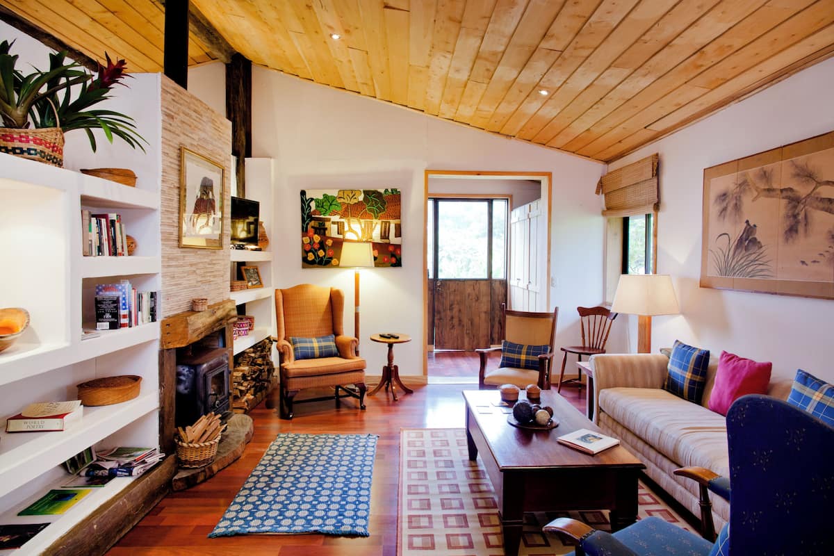 Una sala de estar acogedora con chimenea, pisos de madera y diversas opciones de asientos, incluyendo un sofá y sillones.