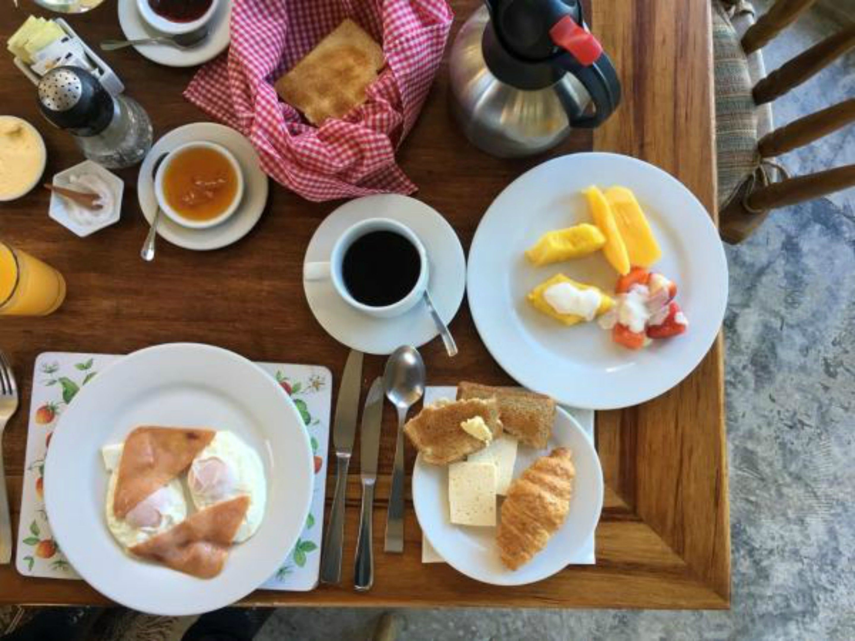 A breakfast tray with eggs, toast, croissants, fruit, and coffee.