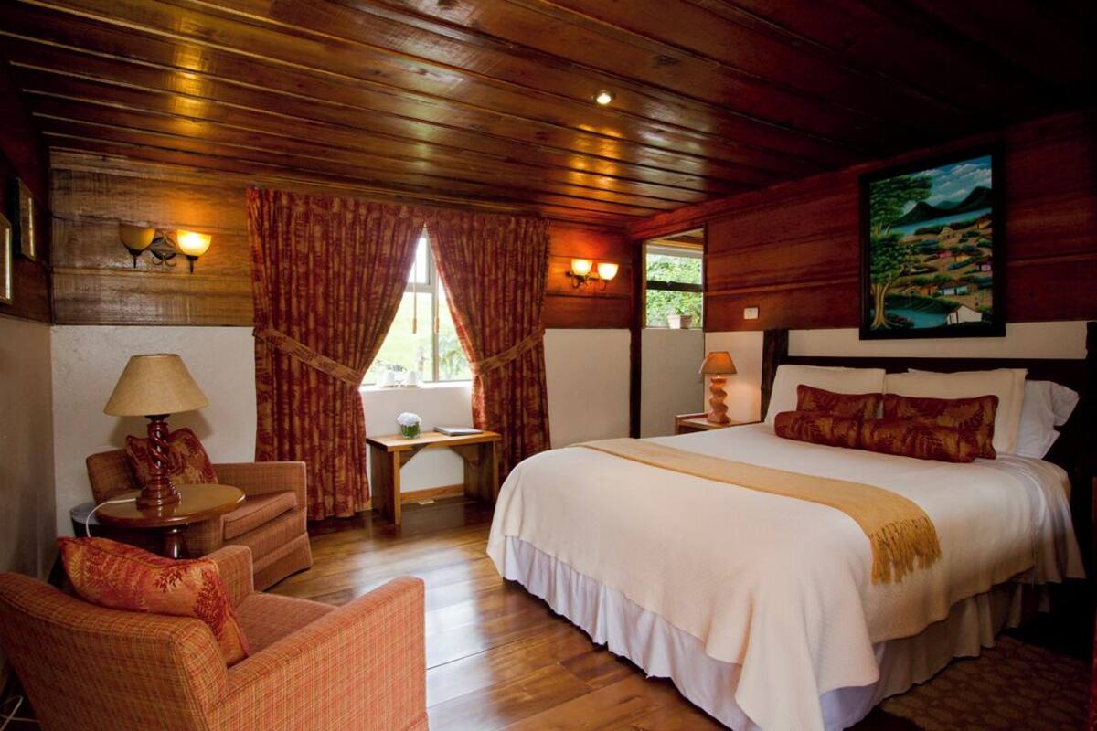 Habitación de cabaña de madera con cama, sofá, escritorio y ventana con cortinas.