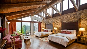 A spacious bedroom with two beds, wooden flooring, stone walls, and large windows.