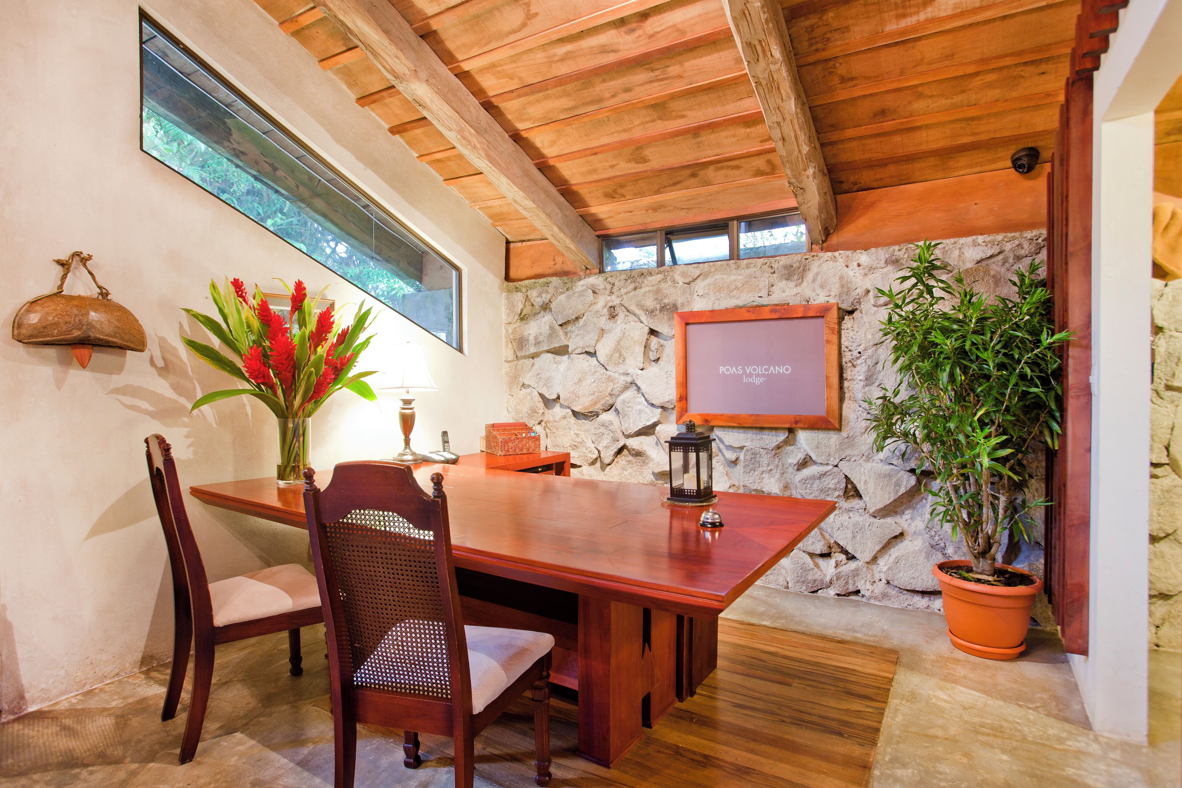 A wooden dining table with chairs, a vase of flowers, a lantern, and a stone wall.