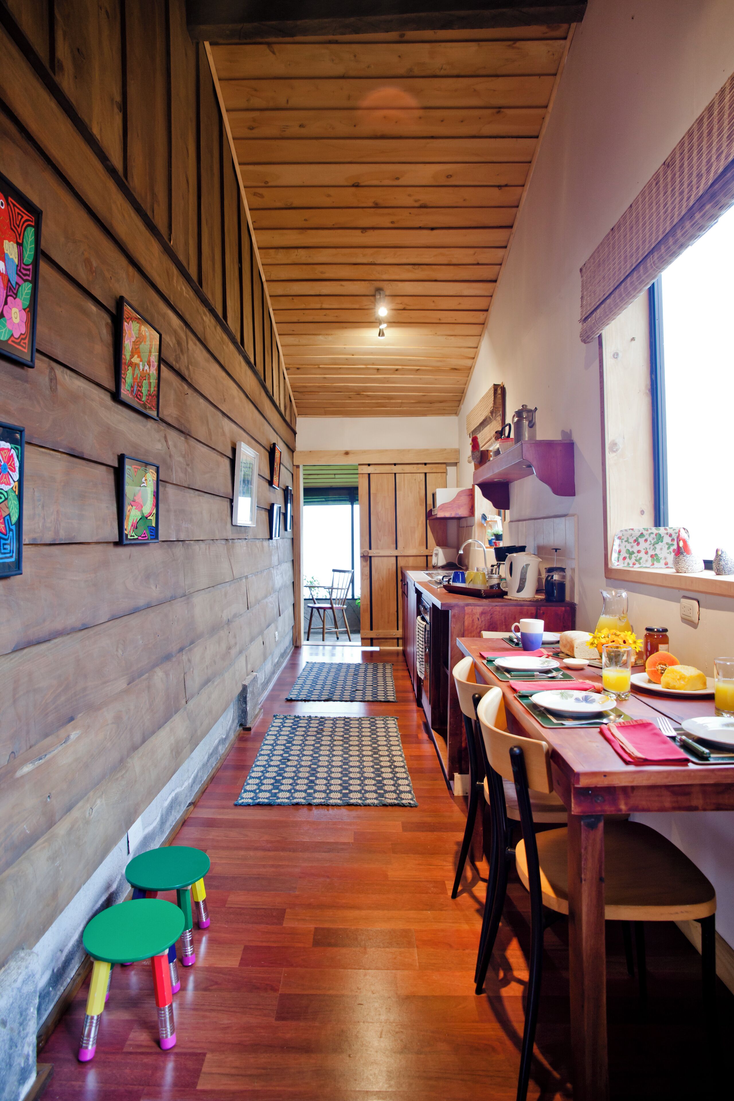 A wooden interior with a dining area, wooden walls, and colorful stools.