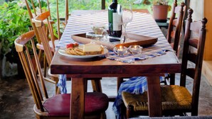 A wooden dining table set with plates, glasses, and a bottle, surrounded by chairs with cushions.