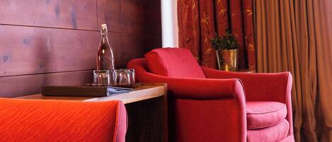 A room with wooden panel walls, a red sofa, a red armchair, a small table with a bottle, glasses, and a plant.