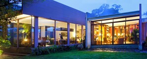 A modern house with large glass windows, a dining area with a table and chairs, and a well-maintained garden. - Poas Volcano Lodge (Vara Blanca)
