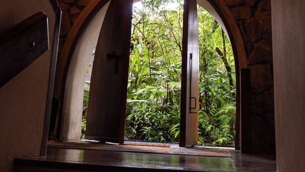 A staircase leading to an arched window with a rustic wooden ceiling and a wheel chandelier.