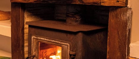 A wood-burning stove with a fire burning inside, set in a stone fireplace.
