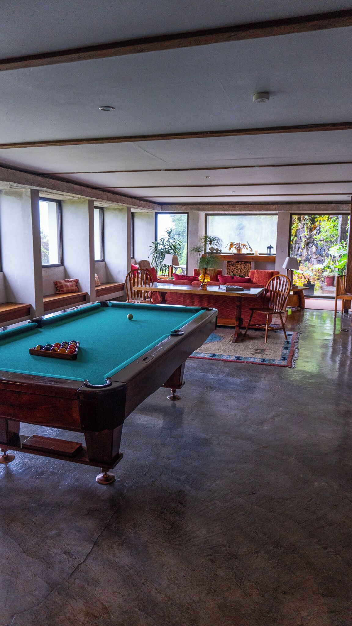 A pool table in a spacious room with large windows, a sofa, and a dining table.