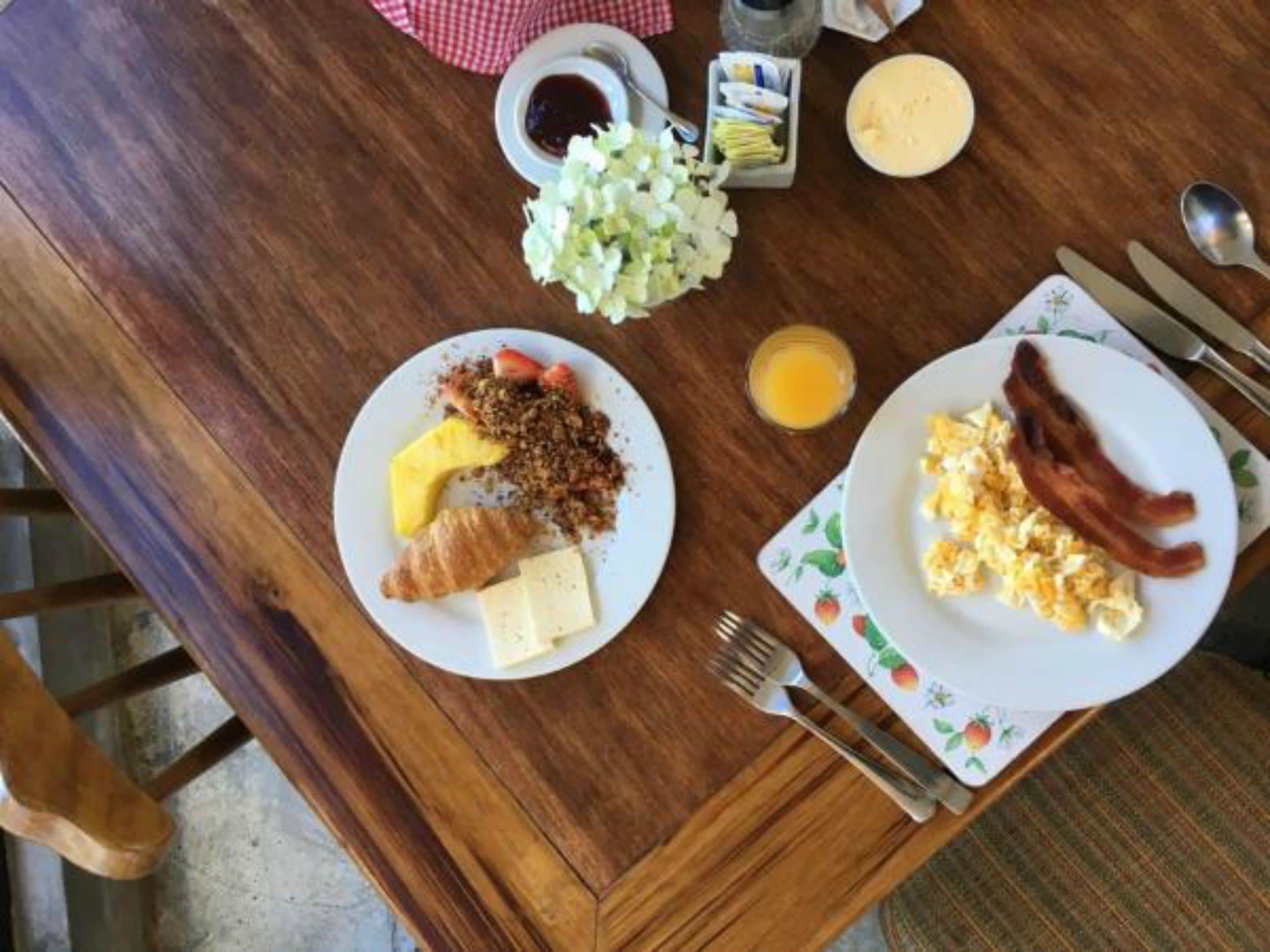 A wooden dining table with breakfast plates, utensils, and condiments.