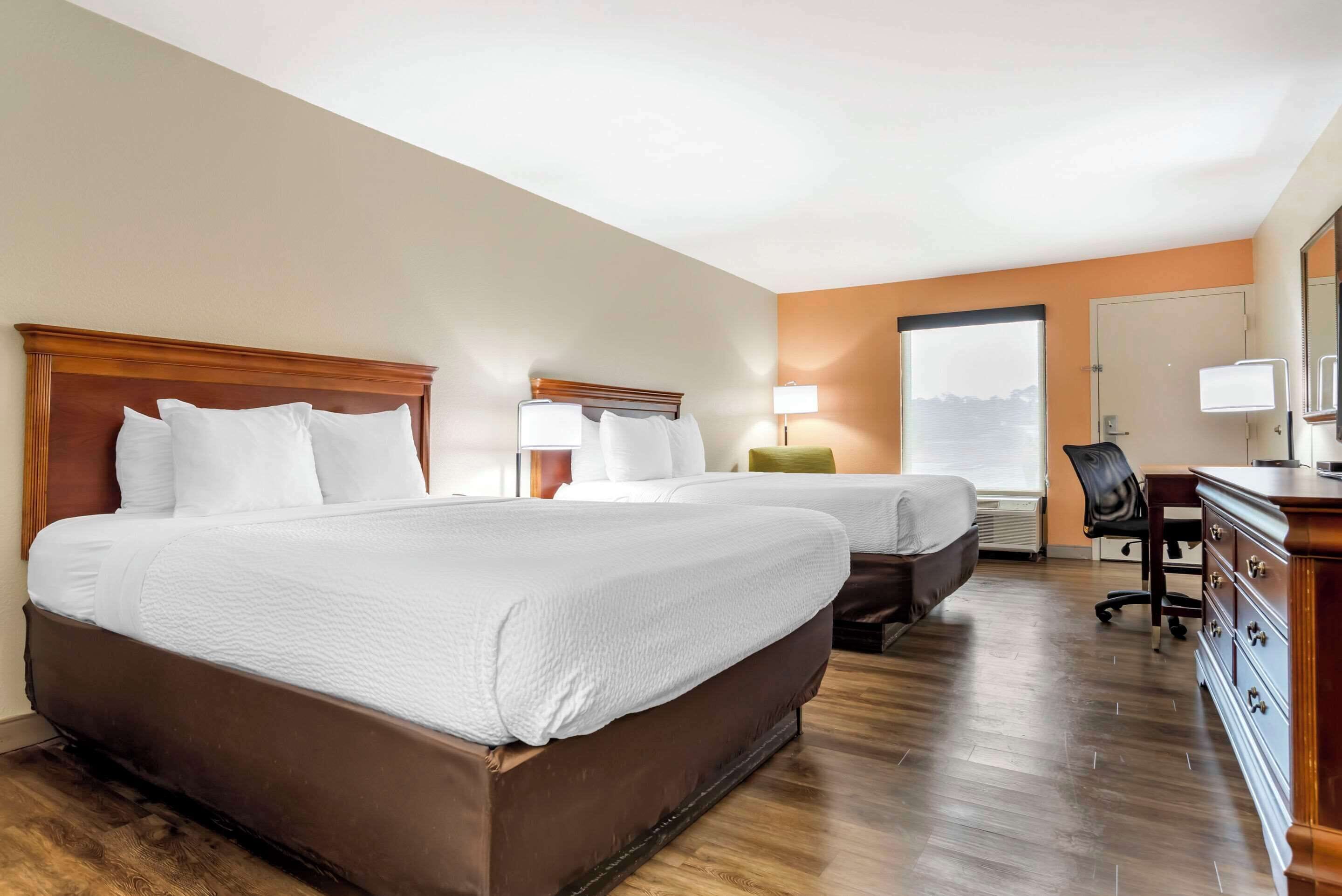 A hotel room with two beds, a desk, a chair, and a dresser.