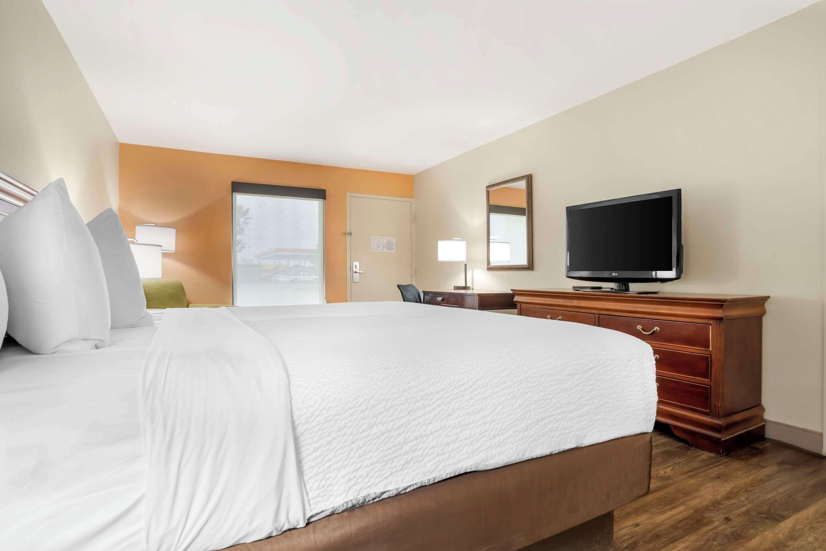 A hotel room with a large bed, a wooden dresser, a television, and a door leading to a balcony.