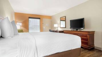 A hotel room with a large bed, a wooden dresser, a television, and a door leading to a balcony.
