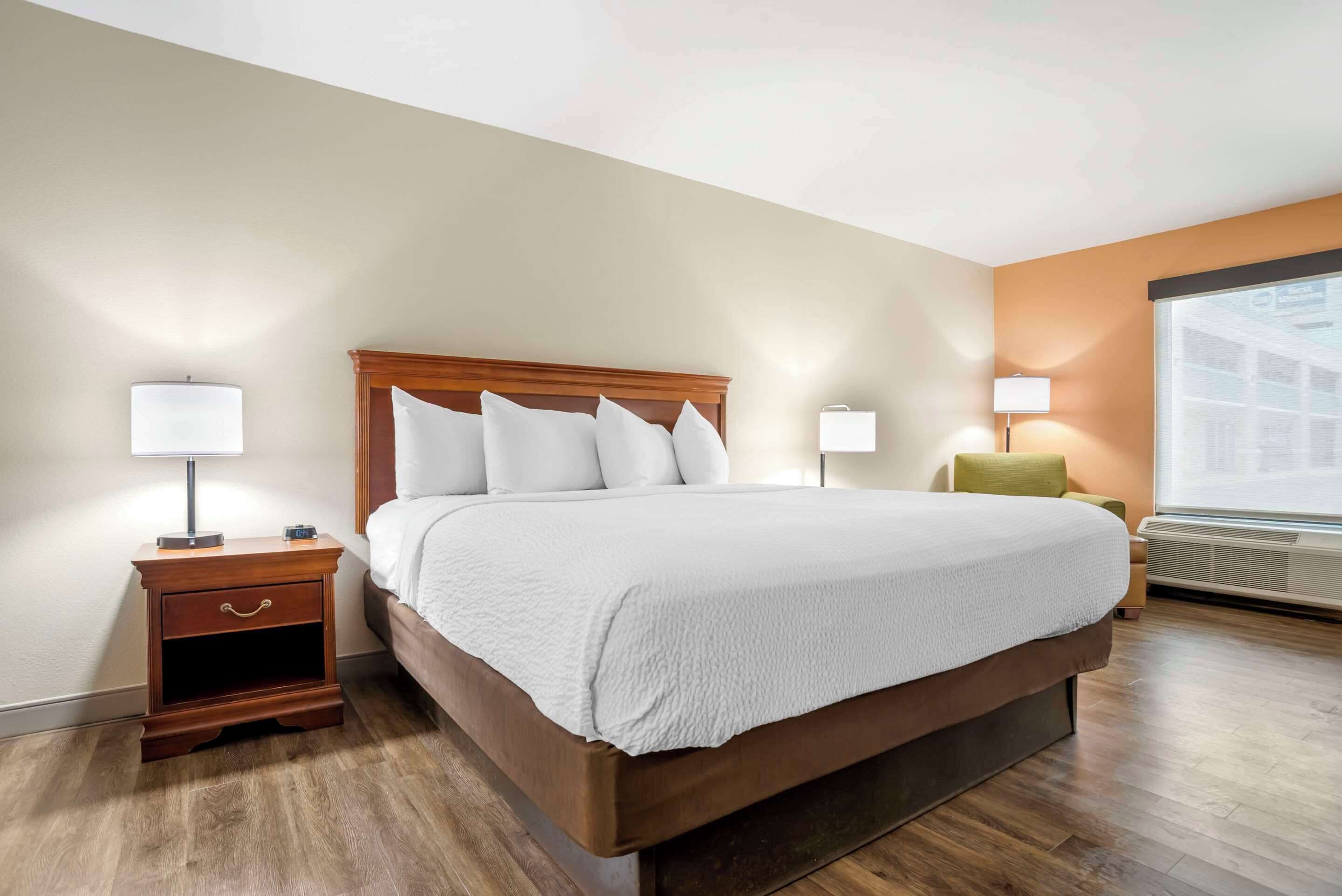 A hotel room with a large bed, wooden nightstand, two bedside lamps, and a window with a view.