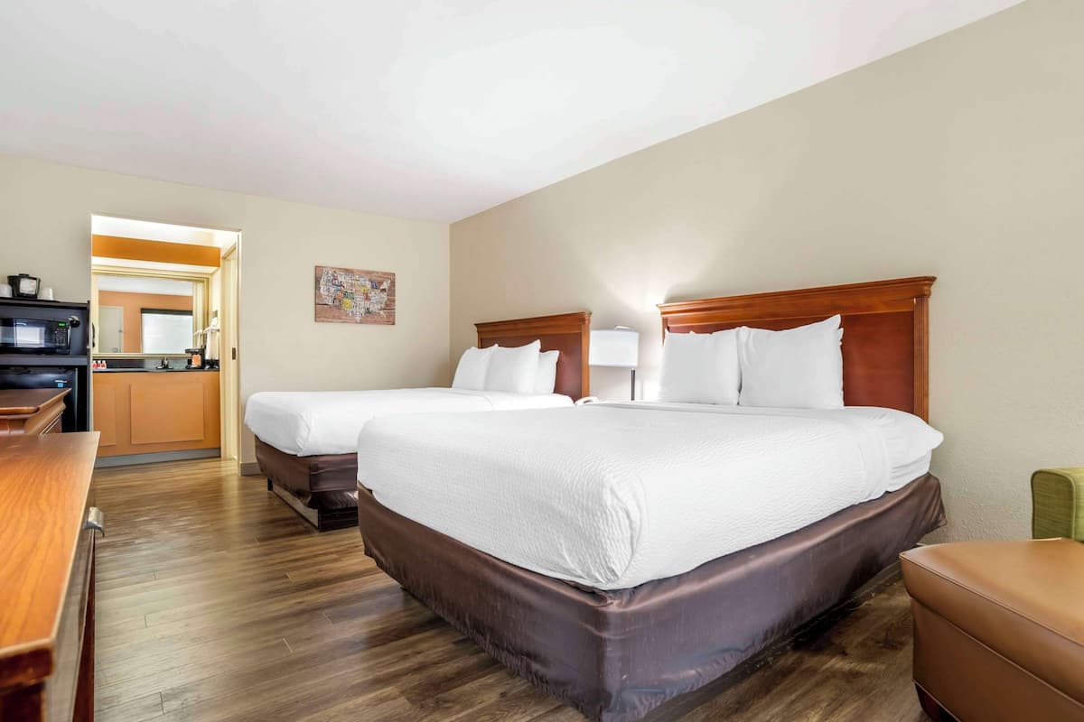 A hotel room with two beds, a wooden desk, and a kitchenette.
