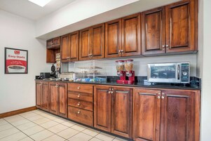 Una cocina con gabinetes de madera, cafetera, microondas y dispensador de cereales.