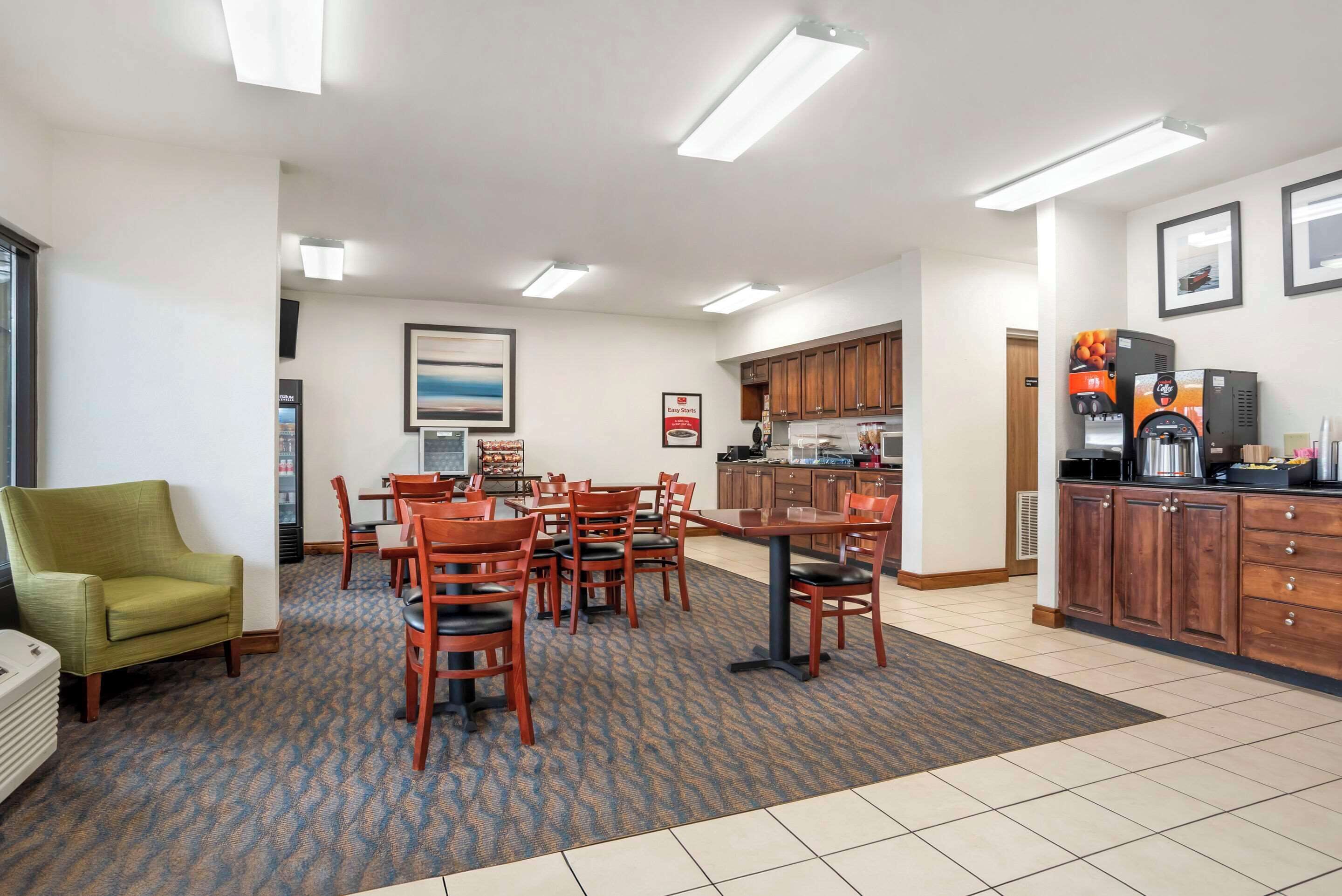 A hotel room with a dining area, kitchenette, and a green armchair.