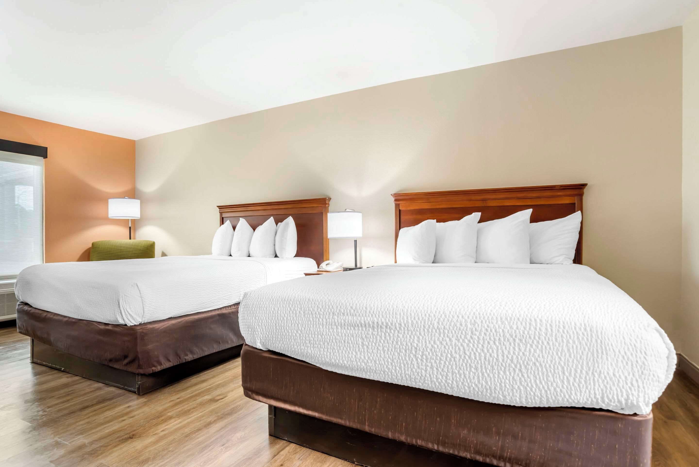 A hotel room with two beds, a green chair, and a lamp.